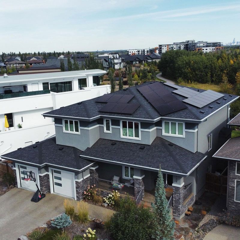 Two-story house with dark solar panels on the roof. Gray exterior with stone accents, located in a suburban neighborhood.