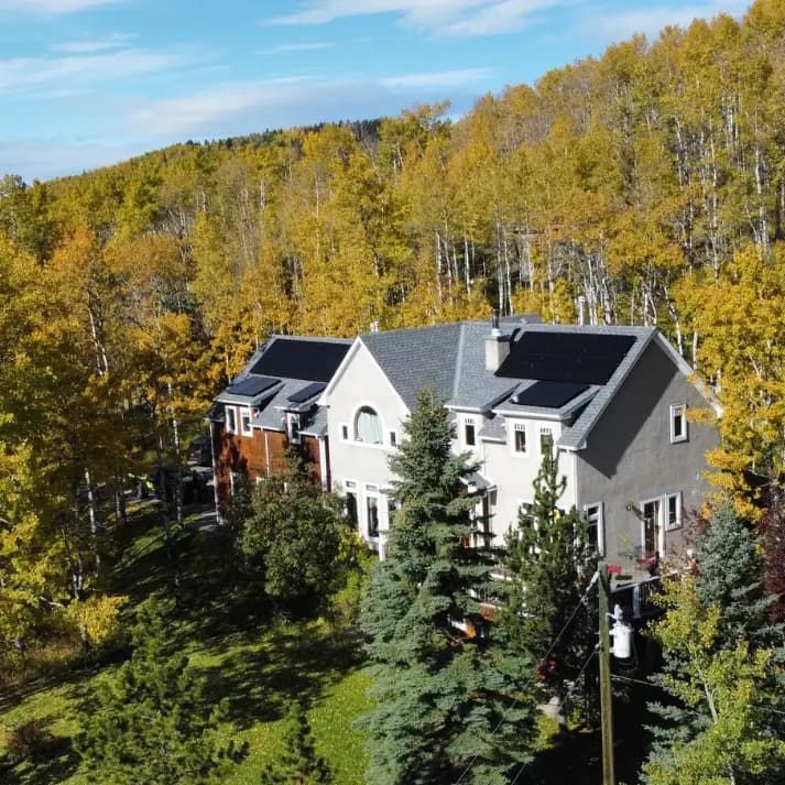 House with solar panels on roof surrounded by golden autumn trees.