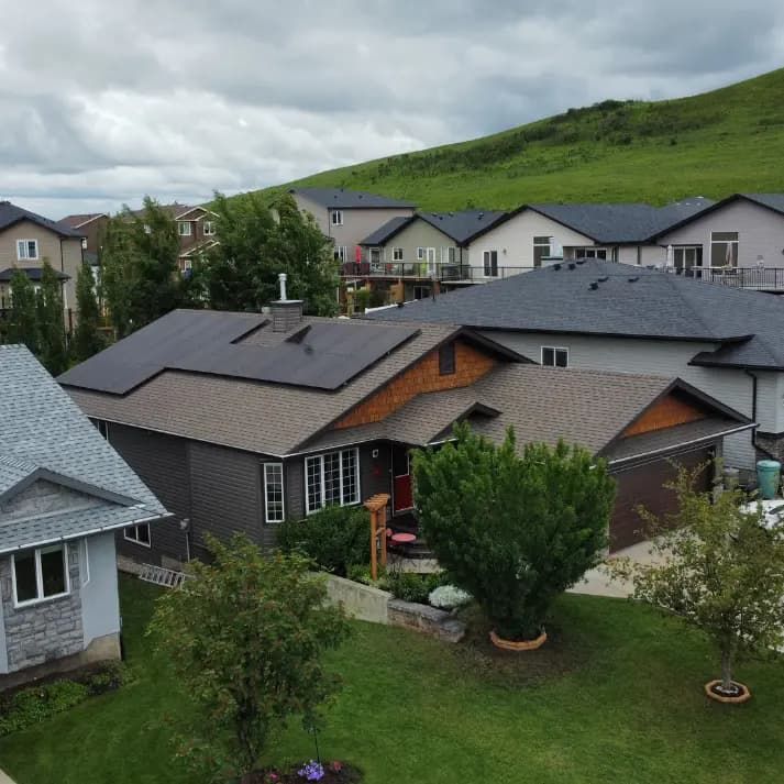 Residential neighborhood with houses, solar panels, and a green hill under a cloudy sky.