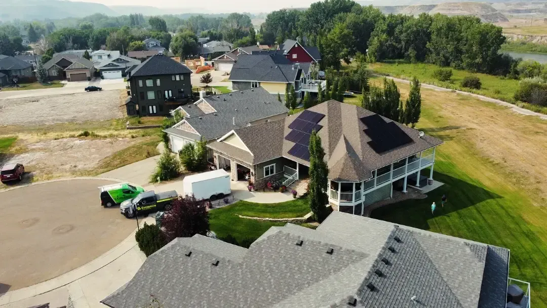 Houses in a neighborhood with solar panels on the rooftops, next to a river and greenery.