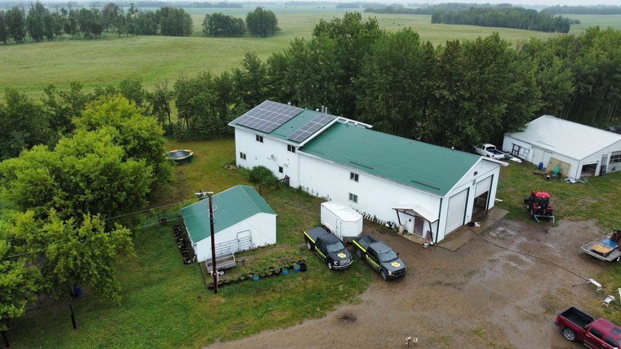 Aerial view of a white building with green roof, surrounded by trees and vehicles. Solar panels on roof.