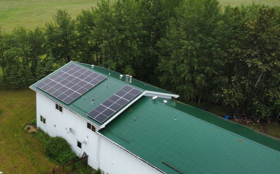 Solar panels on a green metal roof of a white building, set against trees.
