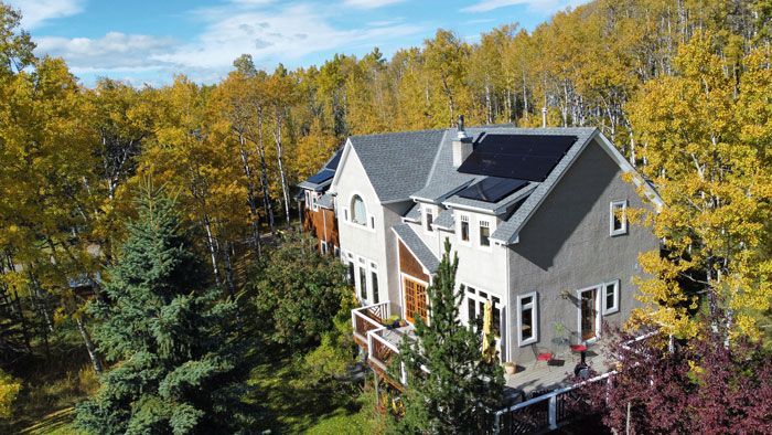 House with solar panels on roof surrounded by autumn trees.