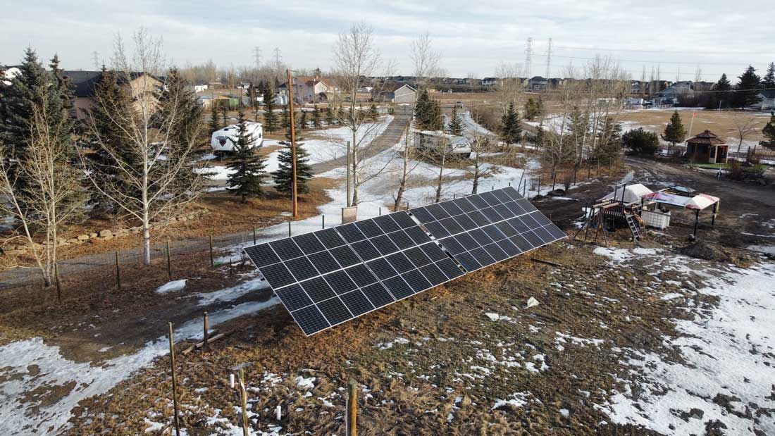 Solar panels on a slight incline in a snow-covered field, houses in the background.