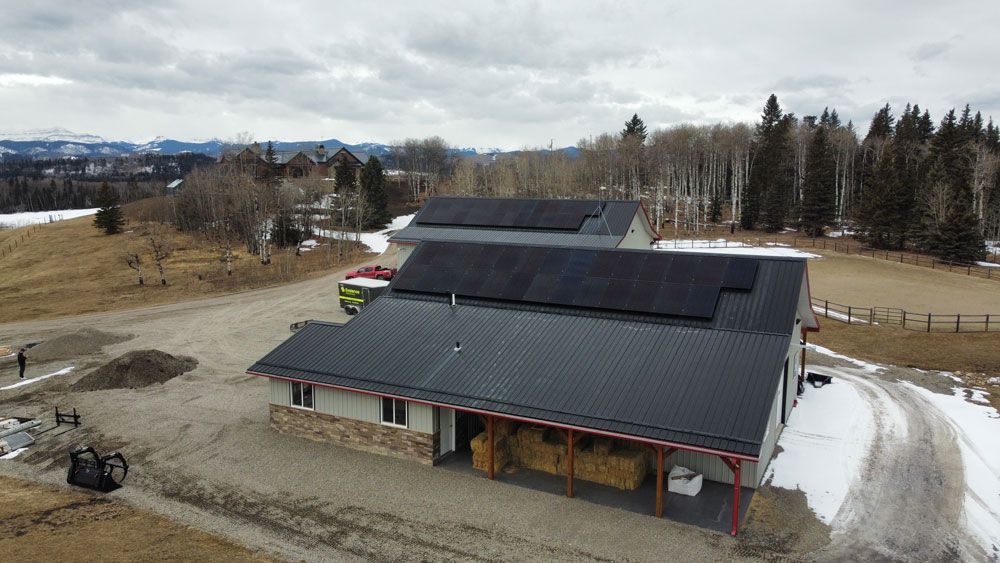 Building with solar panels on roof, open field, trees and mountains in background.