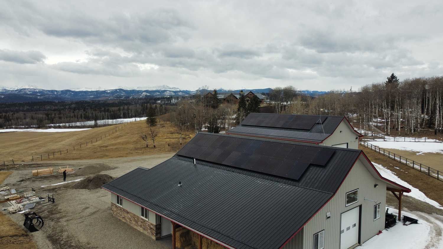 Building with solar panels on roof, field, mountains in background, cloudy sky.