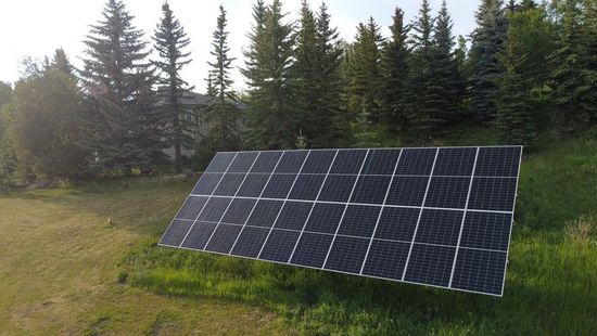 Aerial view of a house with solar panels on a dark gray roof, surrounded by trees and neighboring homes.