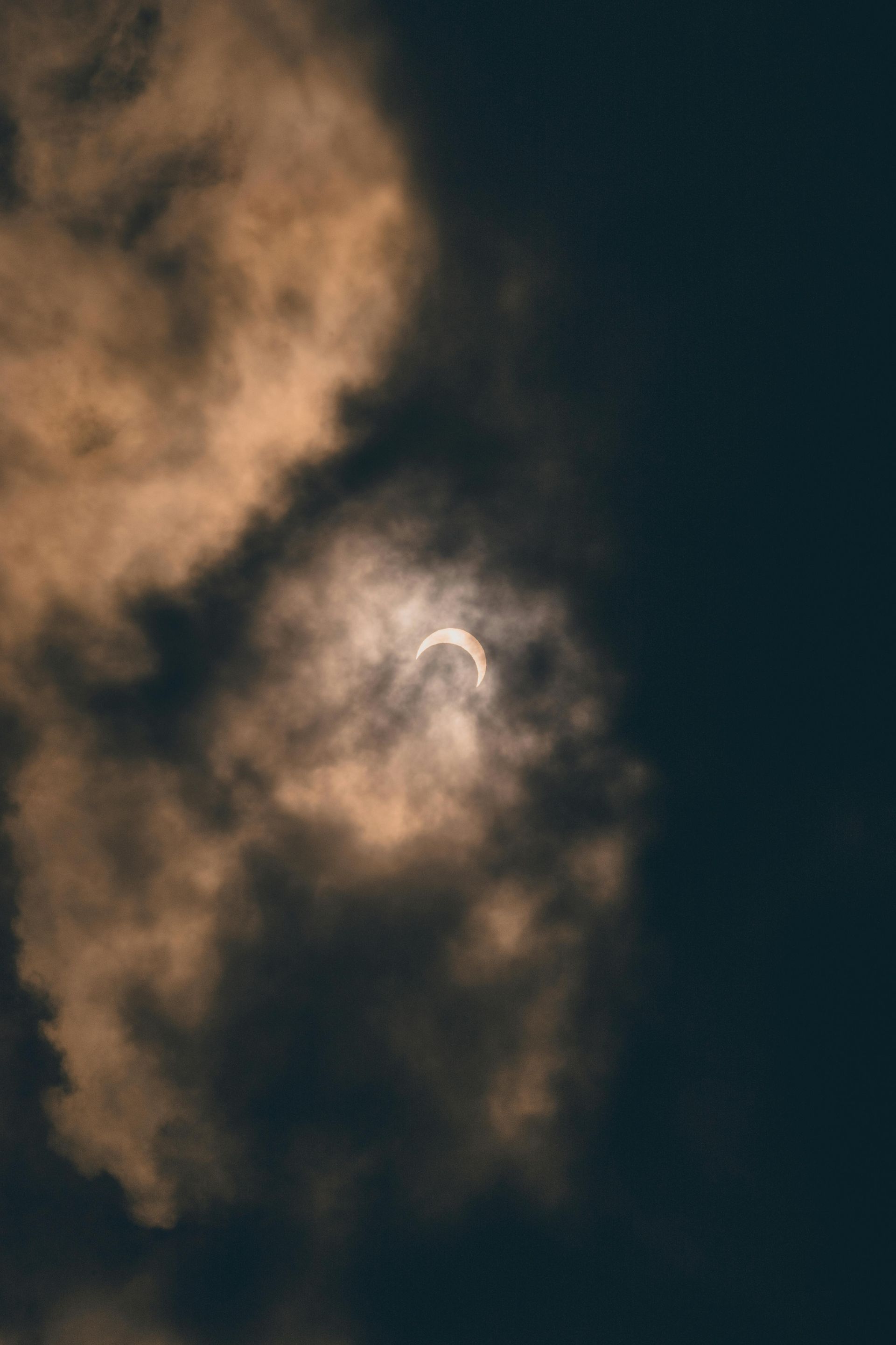 A partial solar eclipse shines through thick, golden-brown clouds against a dark sky.