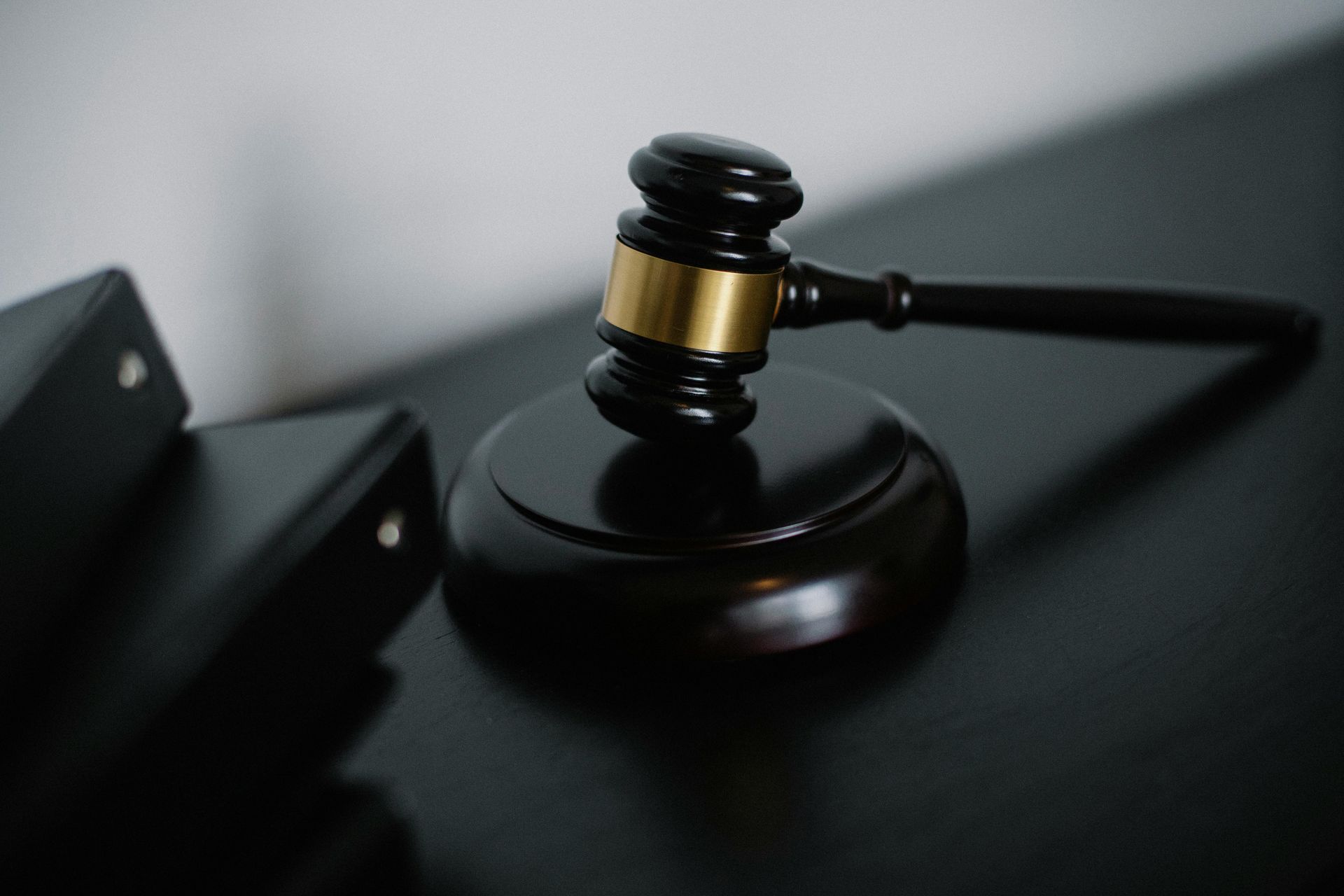 Gavel with brass band resting on a wooden block, near folders on a dark surface.