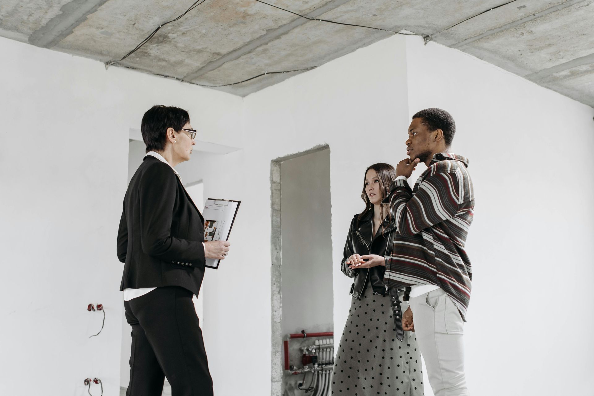 Real estate agent showing unfinished interior to a couple, discussing details.