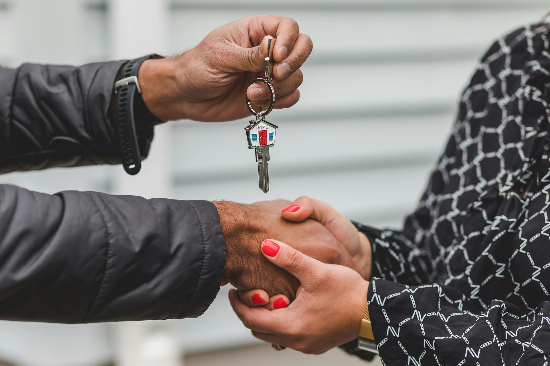 Person handing over house keys attached to a small house keychain. Handshake.