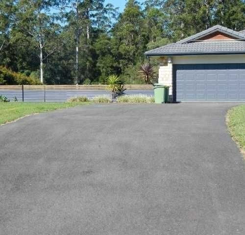 A Driveway Leading to a House with a blue Garage door — Roll Formed Driveways in Yandina, QLD