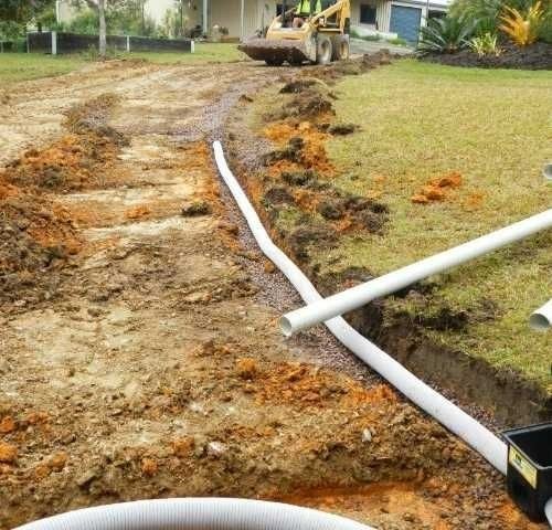 A White pipe is laying in the dirt next to a Yellow Bulldozer — Roll Formed Driveways in Yandina, QLD