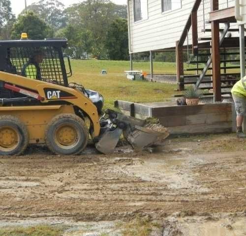 A Man Is Digging in The Dirt Next to A Cat Bulldozer — Roll Formed Driveways in Yandina, QLD