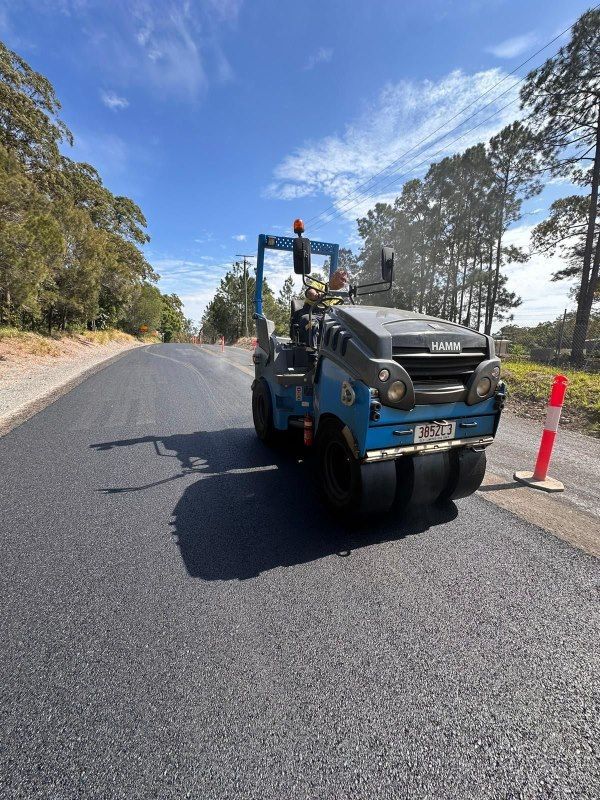 A road roller is driving down a road next to a orange and white cone — Roll Formed Driveways in Yandina, QLD