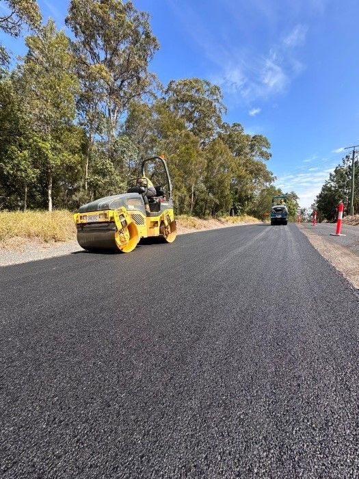 A Yellow And Black Road Roller Is Driving Down A Road — Roll Formed Driveways in Sunshine Coast, QLD
