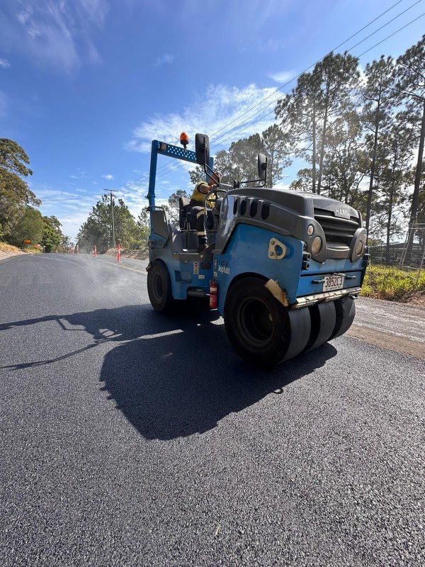 A Blue Roller Is Driving Down A Road With Trees In The Background — Roll Formed Driveways in Noosa, QLD