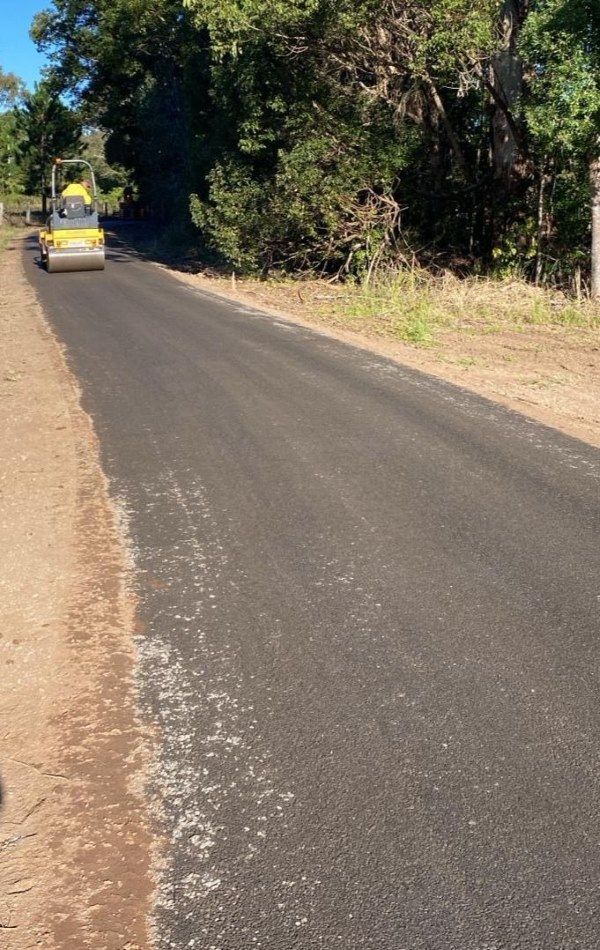 A yellow machine is driving down a road next to trees — Roll Formed Driveways in Noosa, QLD
