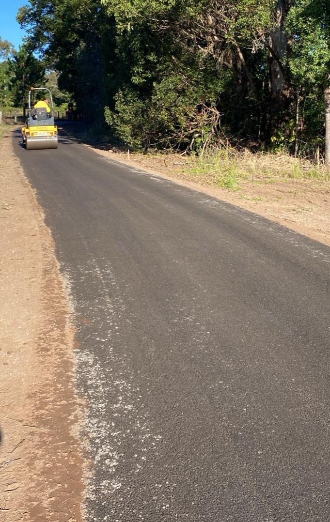 A Car Is Driving Down A Road Next To Trees — Roll Formed Driveways in Yandina, QLD