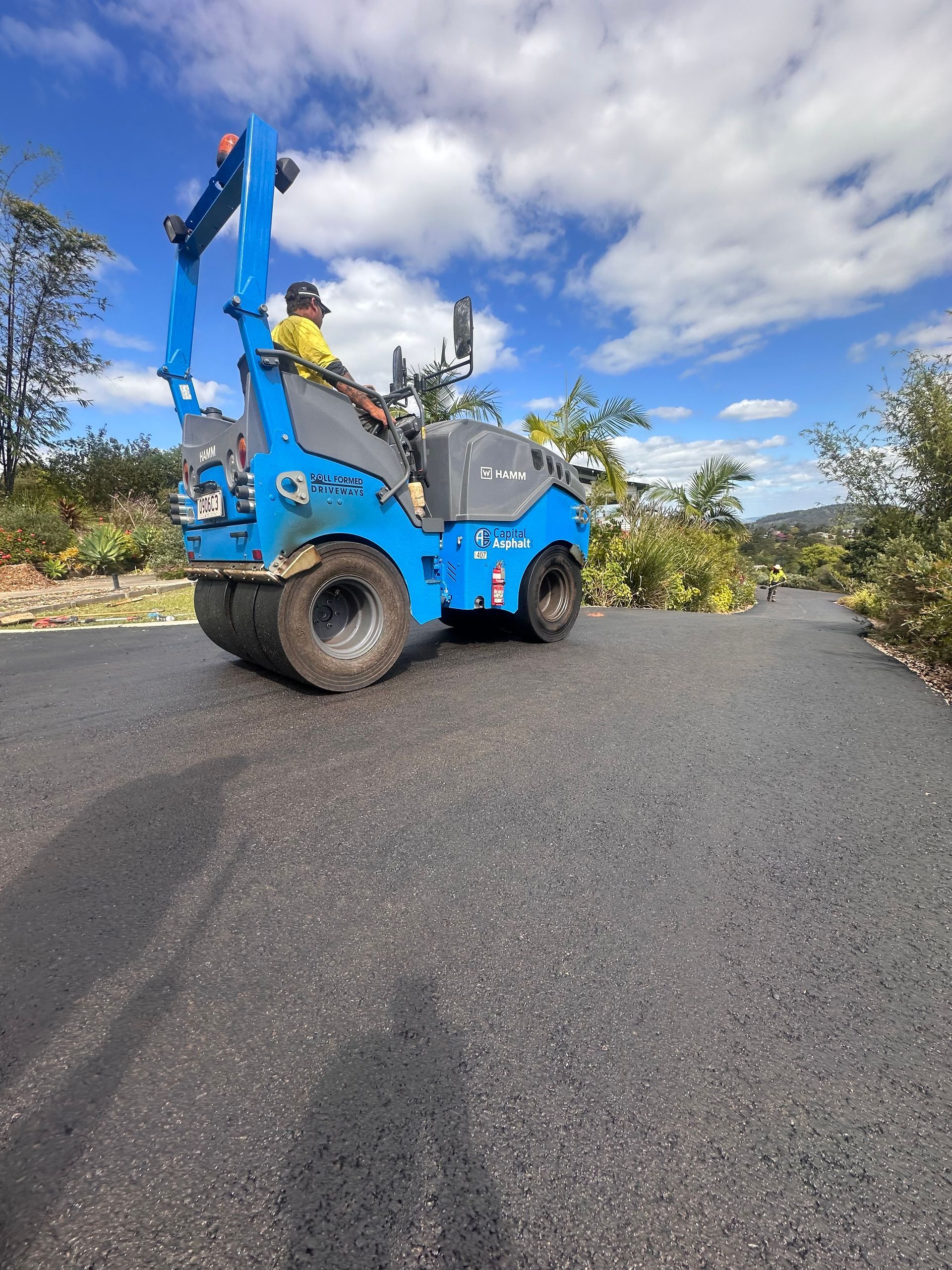 A Man Is Driving A Blue Roller On A Road — Roll Formed Driveways in Yandina, QLD