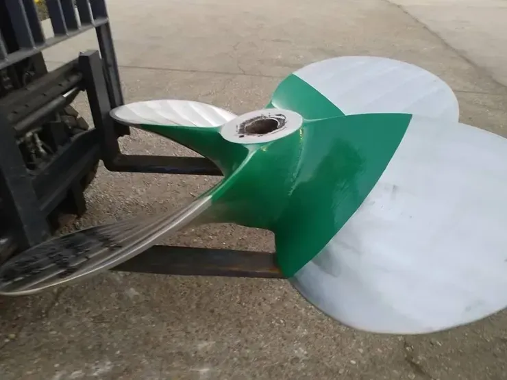 A green and white propeller is being lifted by a forklift