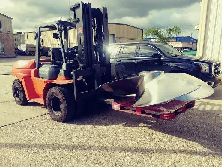A forklift is carrying a large piece of metal on a pallet.