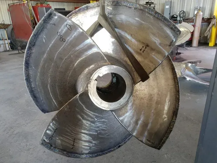 A large metal propeller is sitting on the ground in a warehouse.