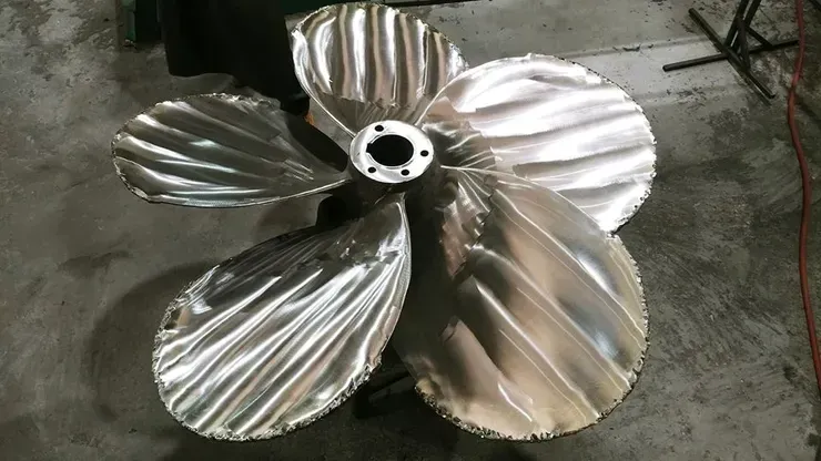 A large stainless steel propeller is sitting on a concrete floor.