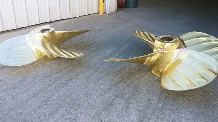 Two brass propellers are sitting on a concrete surface.