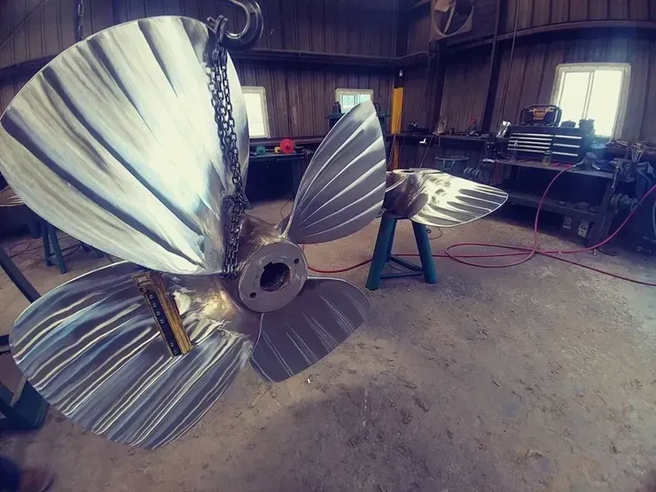 A large metal propeller is hanging from a chain in a room.