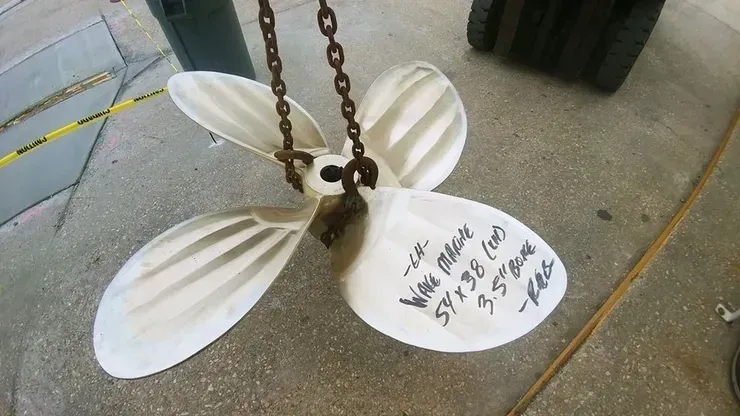 A white propeller is hanging from a chain on the ground.