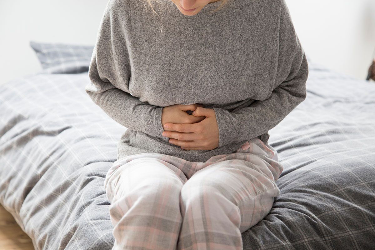 Person sitting on a bed, hunched over and clutching their stomach in pain