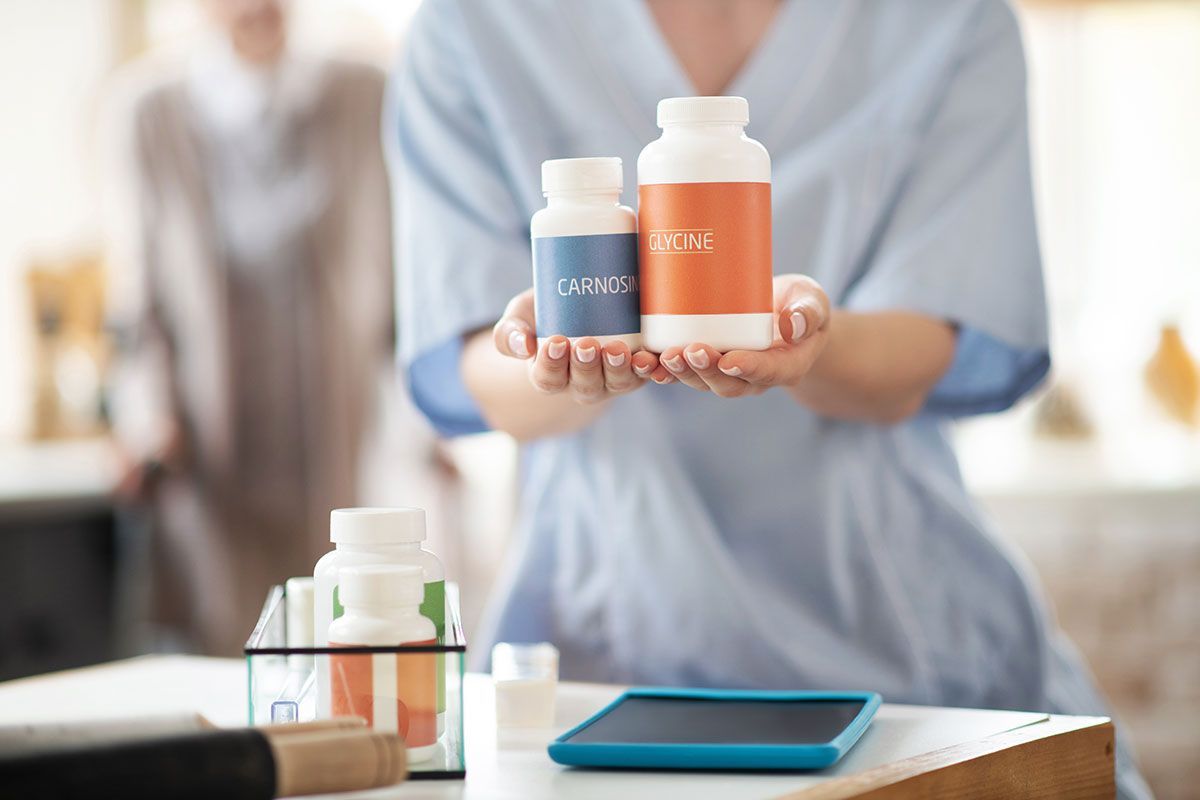 Person holding orange and blue skincare bottles above a table with a tablet and product display