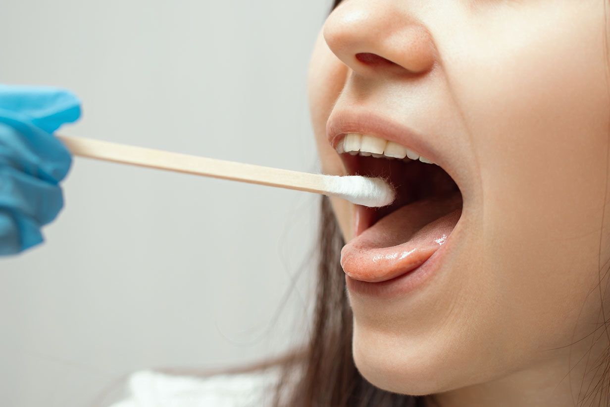 Gloved hand swabbing inside a person’s open mouth for a medical test