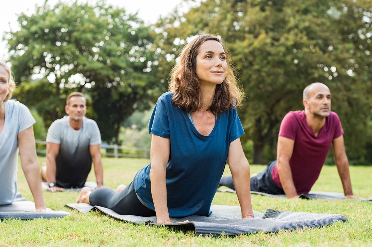 People doing yoga outdoors on mats in a grassy park