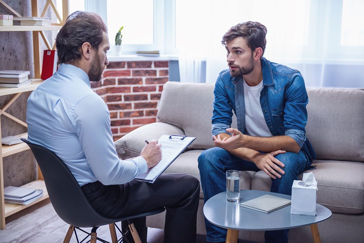 Therapist taking notes while speaking with a client in a bright office.