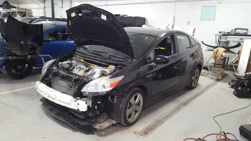 Black car with hood open and front-end damage in a repair shop garage