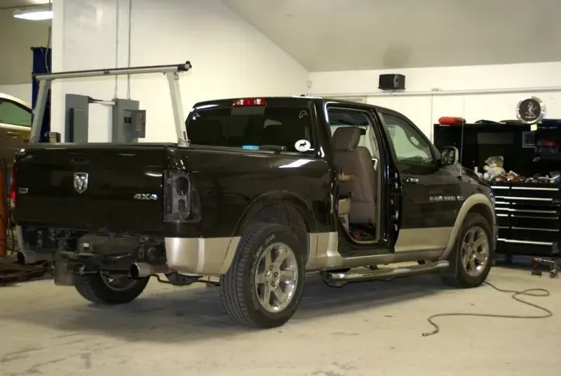 Black pickup truck in an auto shop with the driver door open and equipment around it