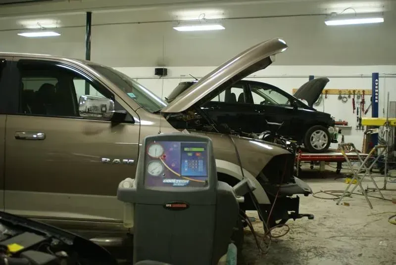 Auto repair shop with two cars, one hood open, and diagnostic equipment in the foreground