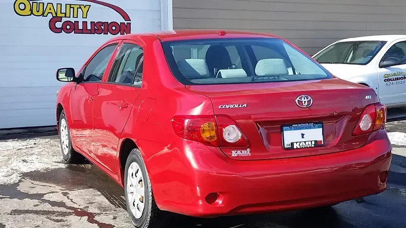 Red Toyota sedan parked outside a collision repair shop on a snowy lot