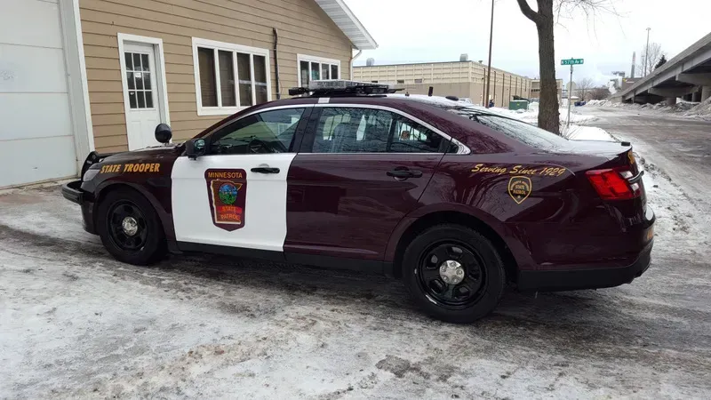 Maroon police cruiser parked on snowy roadside beside a beige building