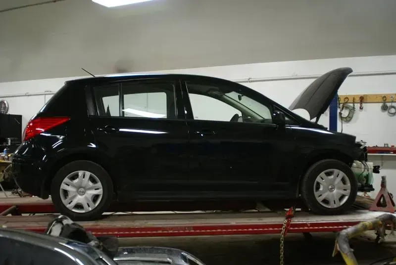 Black hatchback car in an auto repair shop with its hood open on a lift.