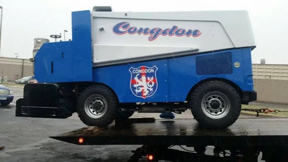 Blue and silver racing-style vehicle on a trailer, with a logo on the side, parked outdoors.