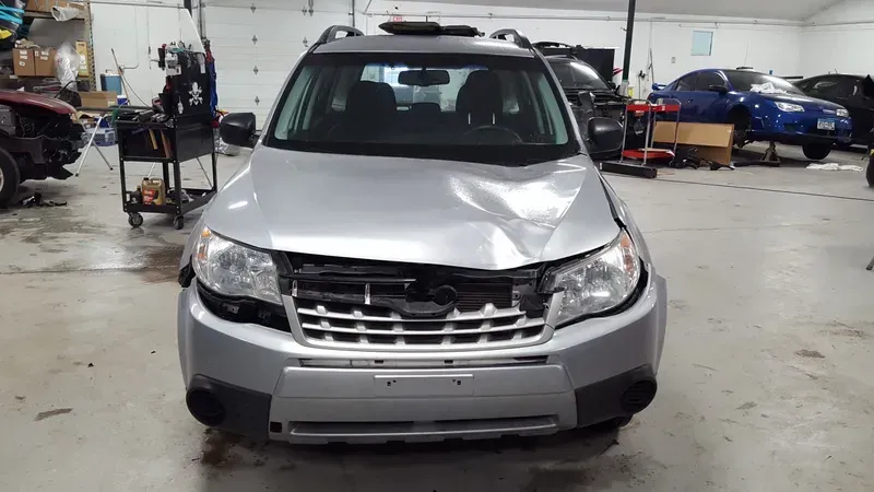 Silver SUV with front-end damage parked in an auto repair shop