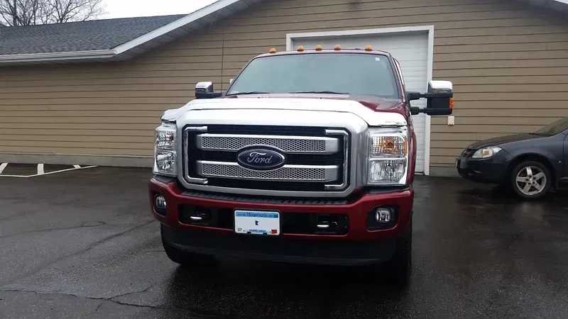 Red Ford pickup truck parked on a wet driveway in front of a tan garage.