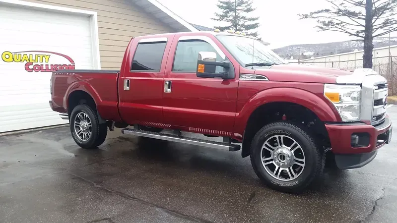 Red Ford crew cab pickup truck parked on a wet lot outside a dealership.