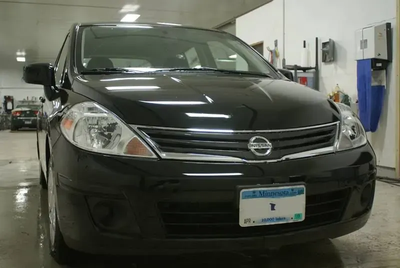 Black Nissan sedan parked indoors in a garage, front view.