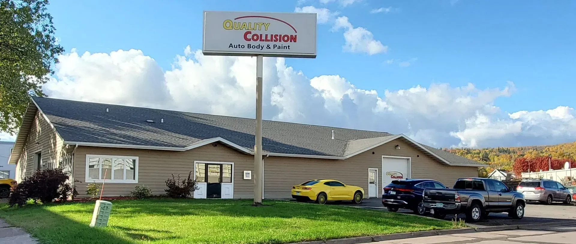 Car dealership lot with a large sign, several parked cars, and a low building under a cloudy sky.