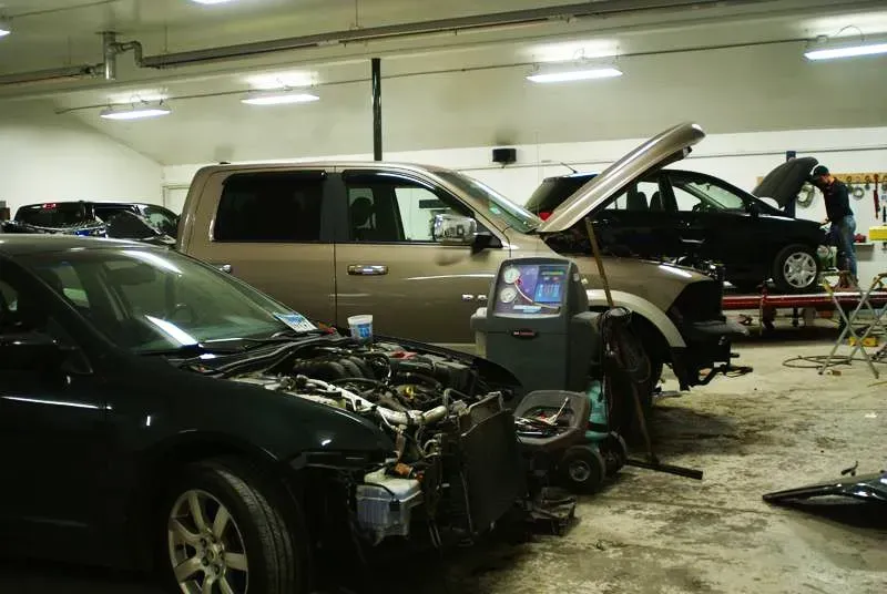 Cars in an auto repair garage, with one hood open and another vehicle under repair.