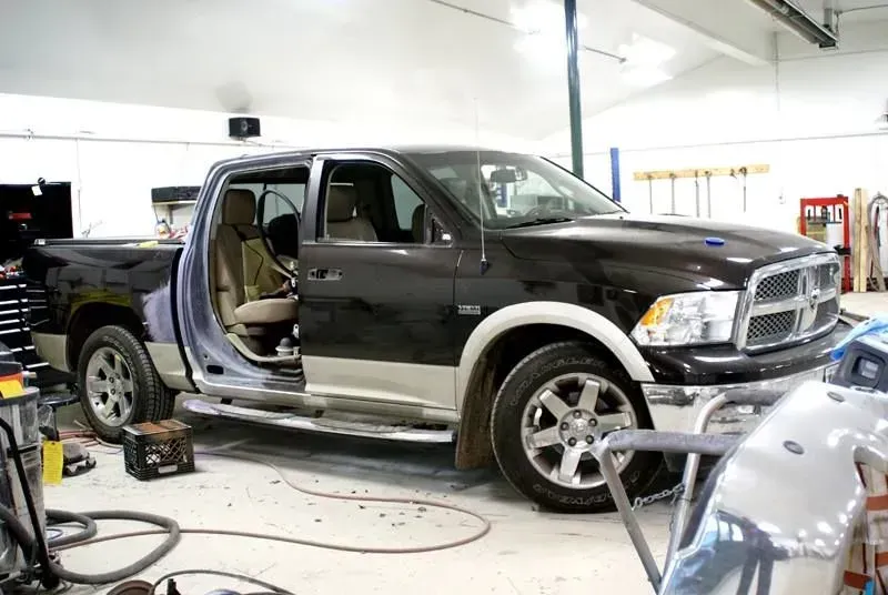 Black pickup truck in an auto shop, with the driver-side doors open and front trim removed during repair.